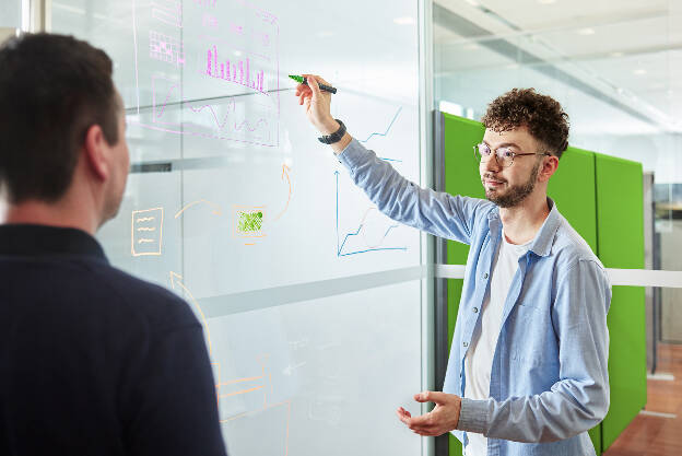 Unternehmensfotografie Unternehmensfoto Mann mit Brille schreibt auf Glaswand und erklärt Diagramme und Skizzen - Businessfotograf Businessfotografie Christian Vorhofer