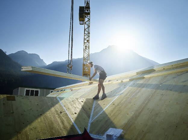 Zimmermann am Dach mit Baustellkran und Bretter im Gegenlicht, Industriefotografie Christian Vorhofer, Kunde WKO Tirol