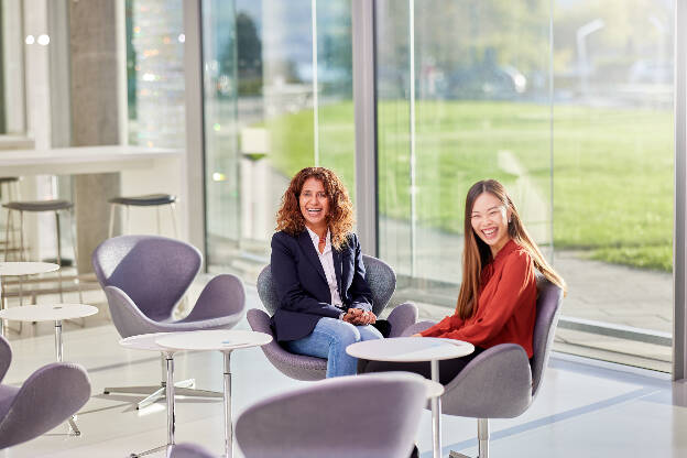 Foto zwei lachende Mitarbeiterinnen in modernem Bürogebäude mit Glasfront Employer Branding - Businessfotograf Businessfotografie Christian Vorhofer