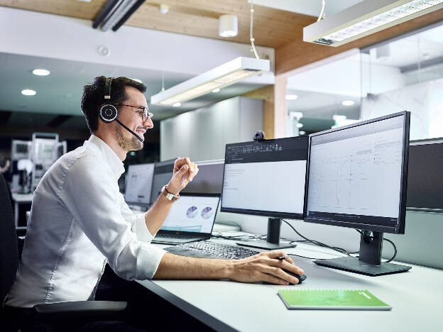 Mann Mitarbeiter sitzt mit Headset und mehreren Bildschirmen am Schreibtisch - Businessfotograf Businessfotografie Christian Vorhofer